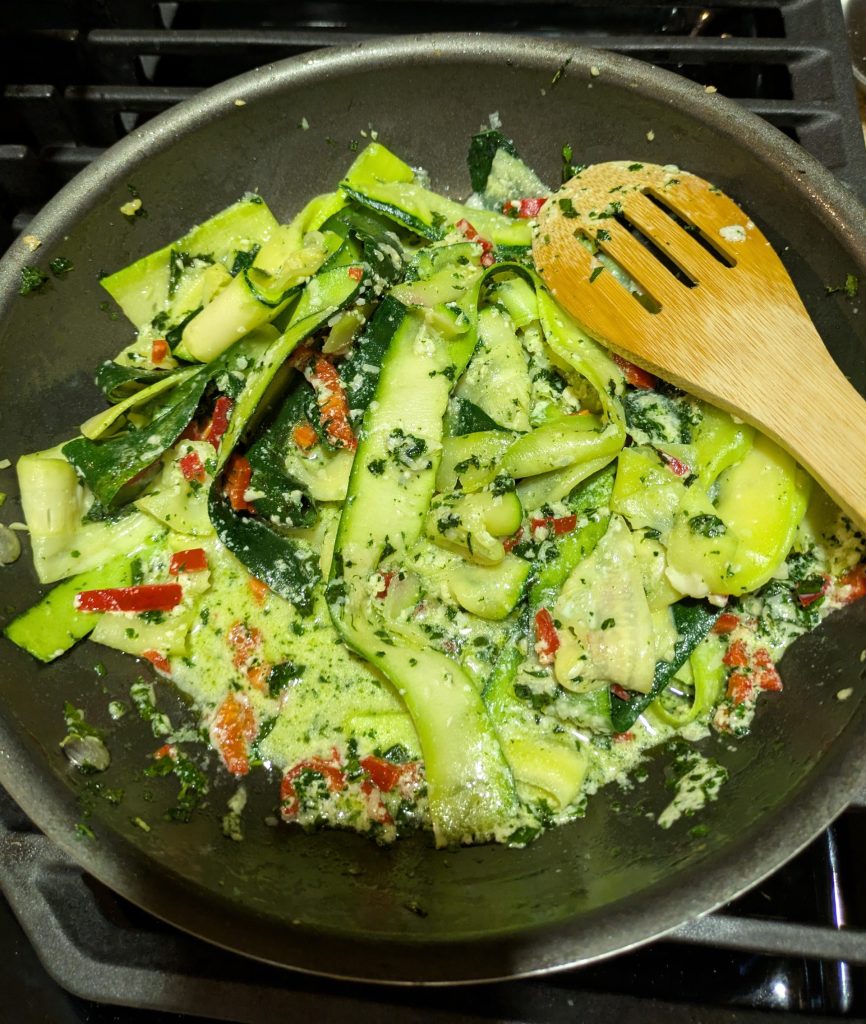 Vibrant vegetable display of sauteed zucchini red chiles and basil in a nonstick skillet with a wooden slotted spoon.